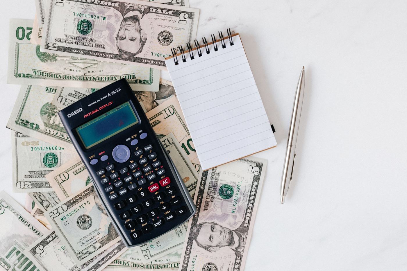 A calculator, notepad and pen resting on a pile of banknotes