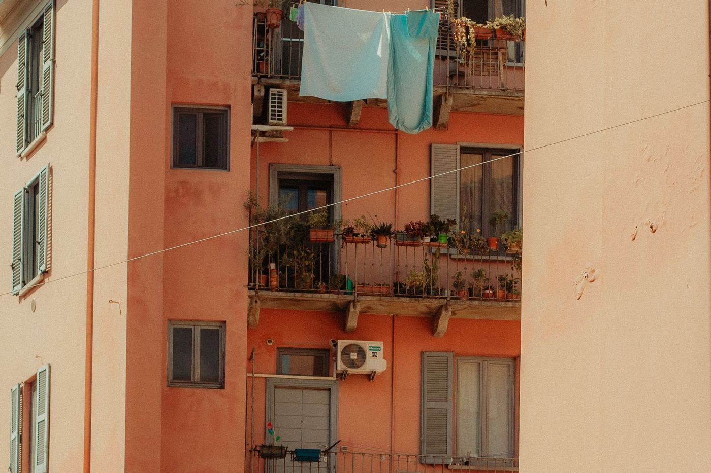 The pink façade of an Italian apartment block with green shutters, balconies and washing lines