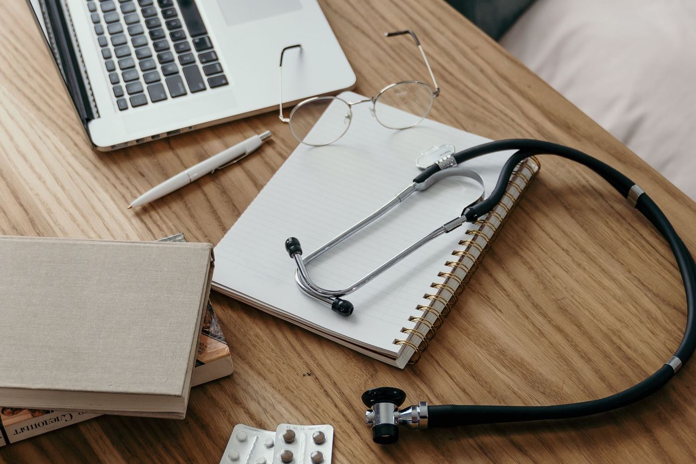 A stethoscope, notebook and medication on a wooden desk
