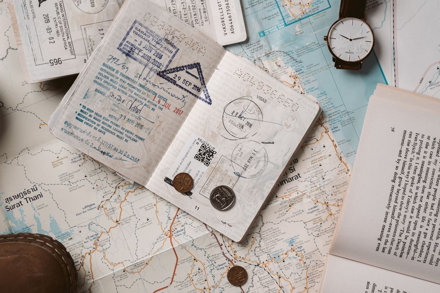An open passport with entry stamps lying on a map beside a wristwatch
