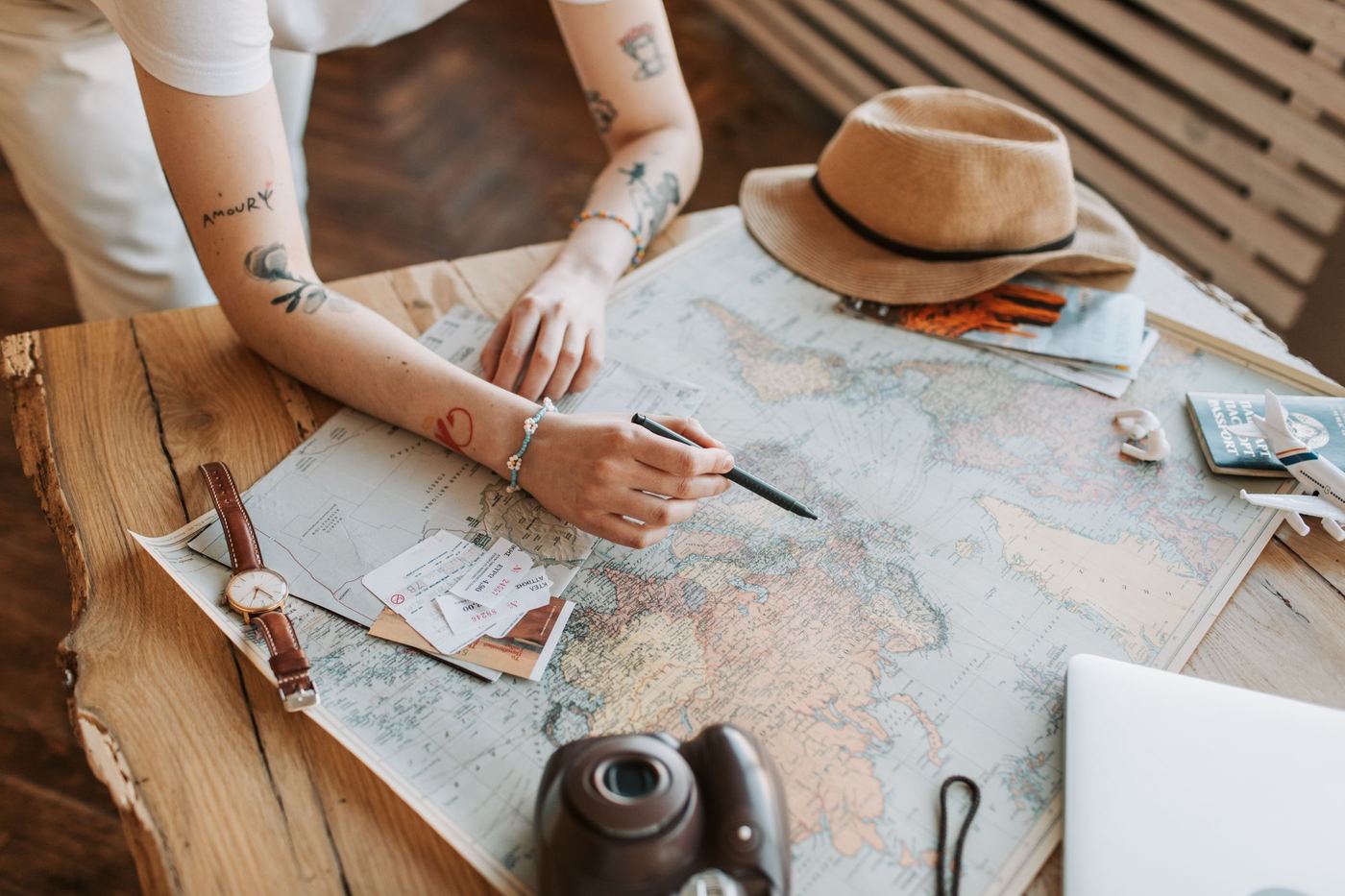 A person tracing a route on a paper world map surrounded by travel items