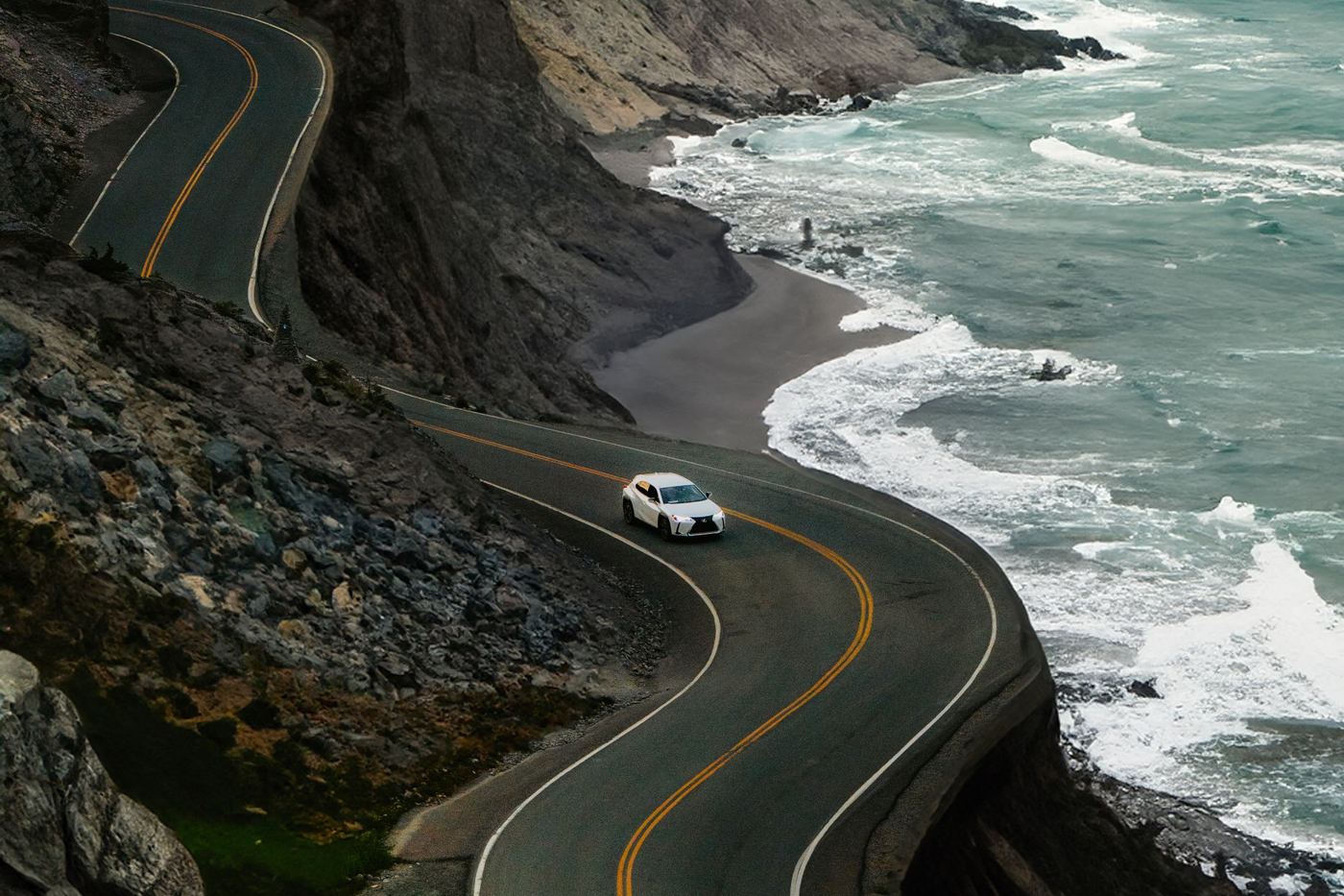 A white car driving along a winding coastal road above the sea