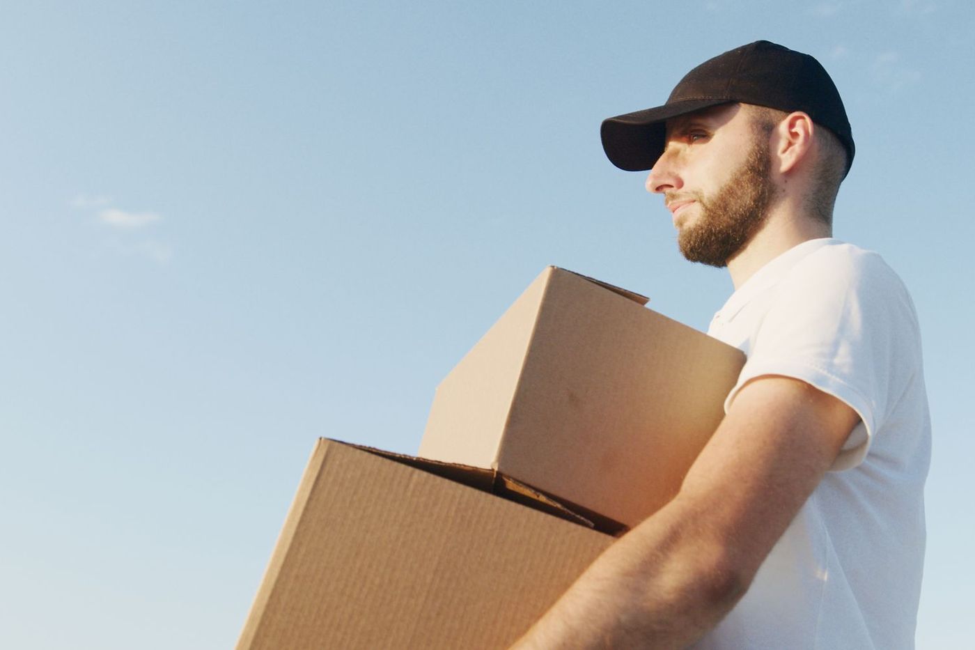 A mover carrying a large cardboard box outdoors against an open sky