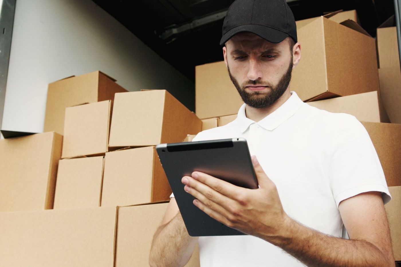 A mover checking an inventory on a tablet beside a wall of cardboard boxes inside a van