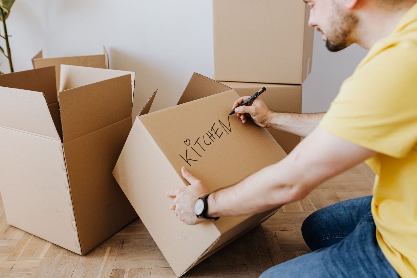 Someone writing the word KITCHEN on a packed cardboard box with a marker pen