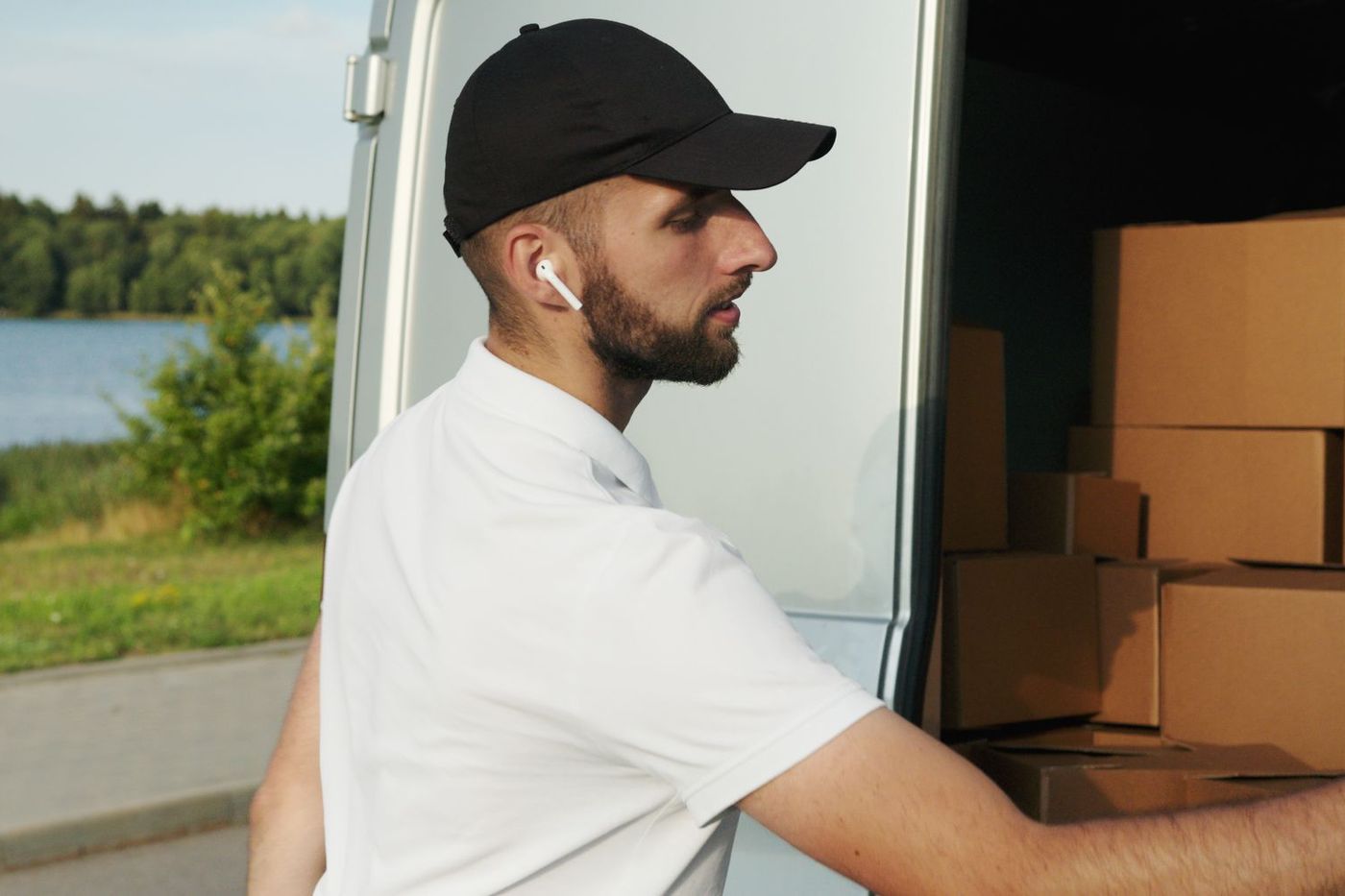 A mover resting against the open side of a loaded van on a quiet road, cardboard boxes stacked behind him